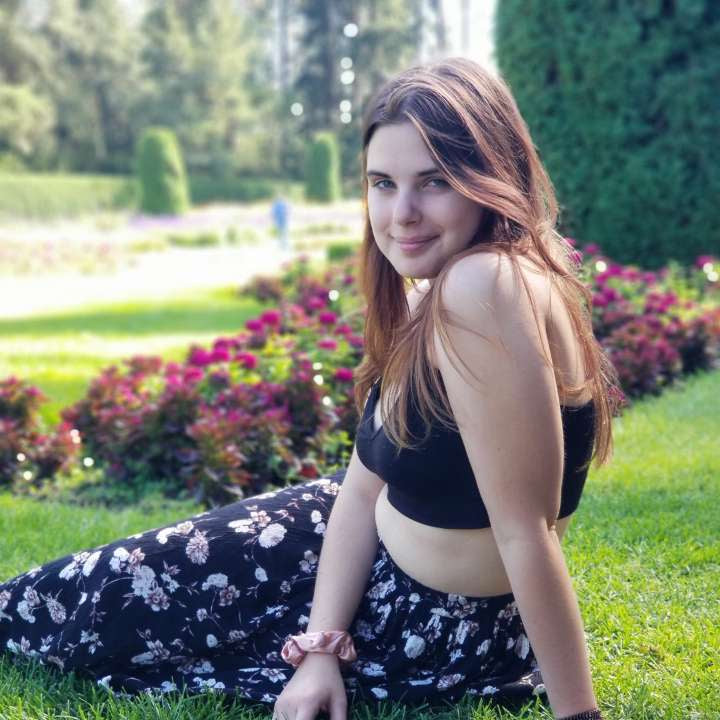 Woman sitting on grass in a park with flowers and trees in the background