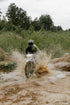 Person riding a motorcycle through muddy water with trees in the background